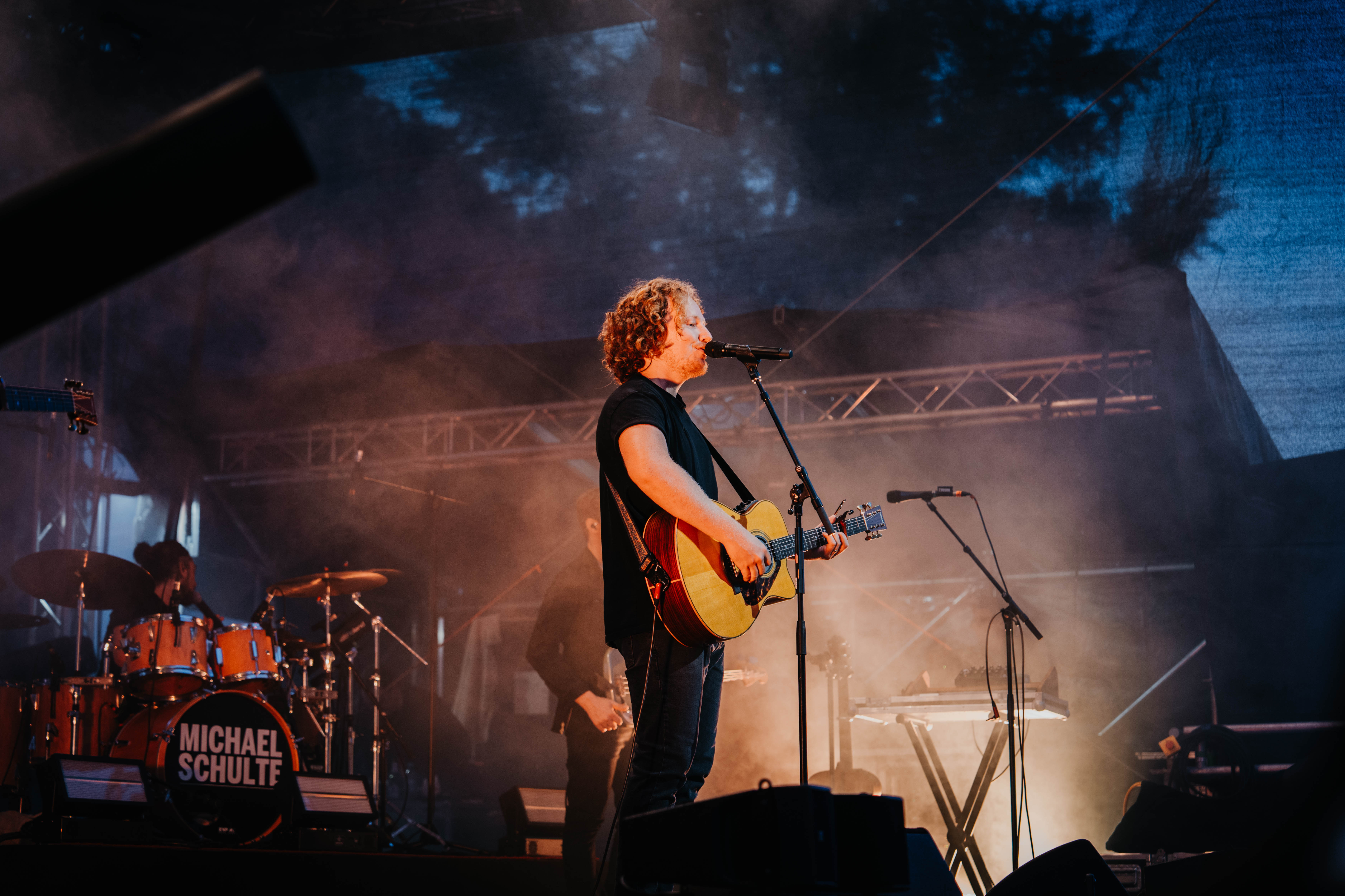 Michael Schulte spielt Gitarre und singt auf einer Bühne mit Nebel und Bühnenbeleuchtung.