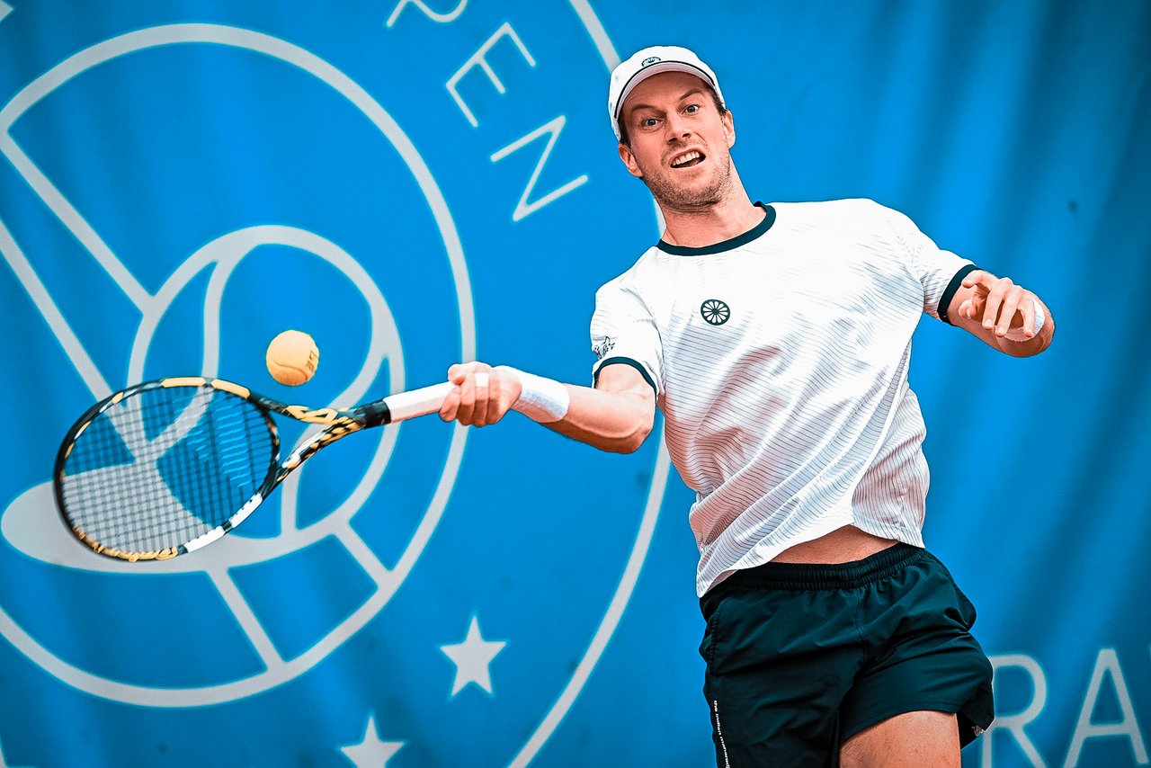 Tennisspieler Botic Van De Zandschulp schlägt einen Vorhandball auf einem blauen Platz mit Turnierlogo im Hintergrund.