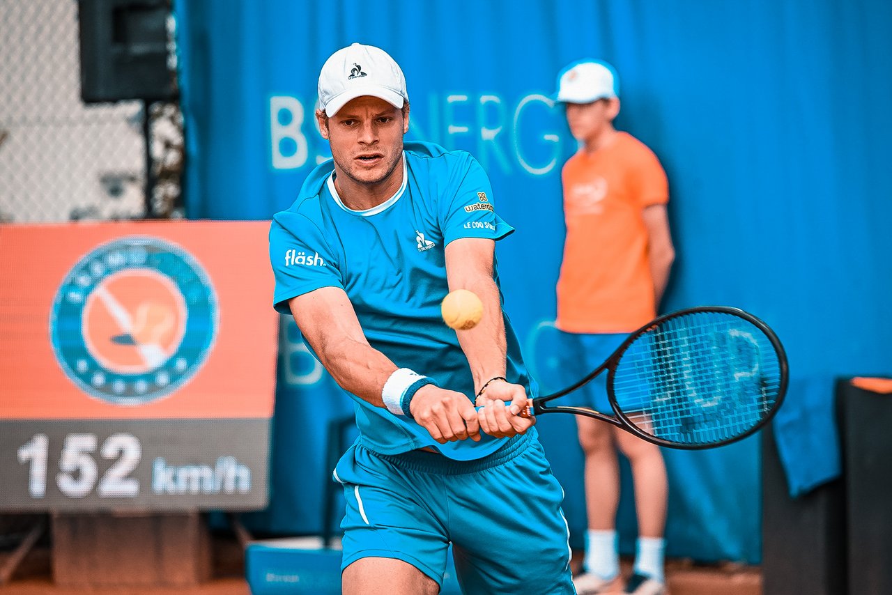 Tennisspieler Yannick Hanfmann schlägt einen Rückhandschlag auf Sandplatz, trägt blaues Sportoutfit und weiße Kappe.